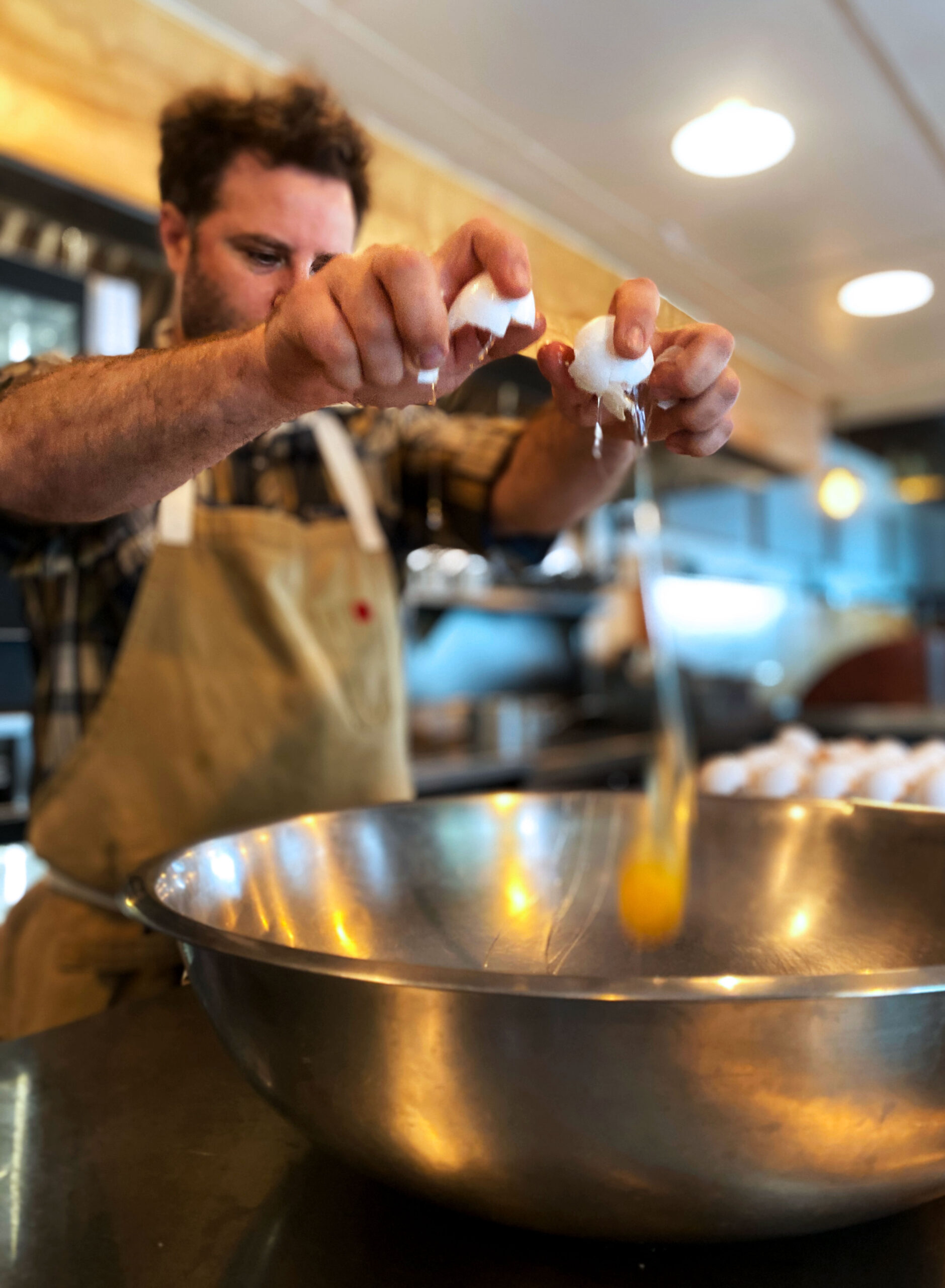 Chef Nathan Lemley cracking eggs over a stainless steel bowl.