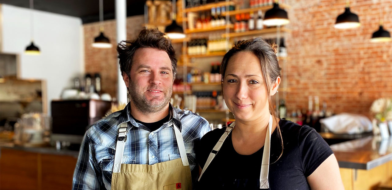 Chef Sarah Heard and Chef Nathan Lemley, owners of Commerce Cafe, standing in their restaurant smiling in Lockhart, Texas.